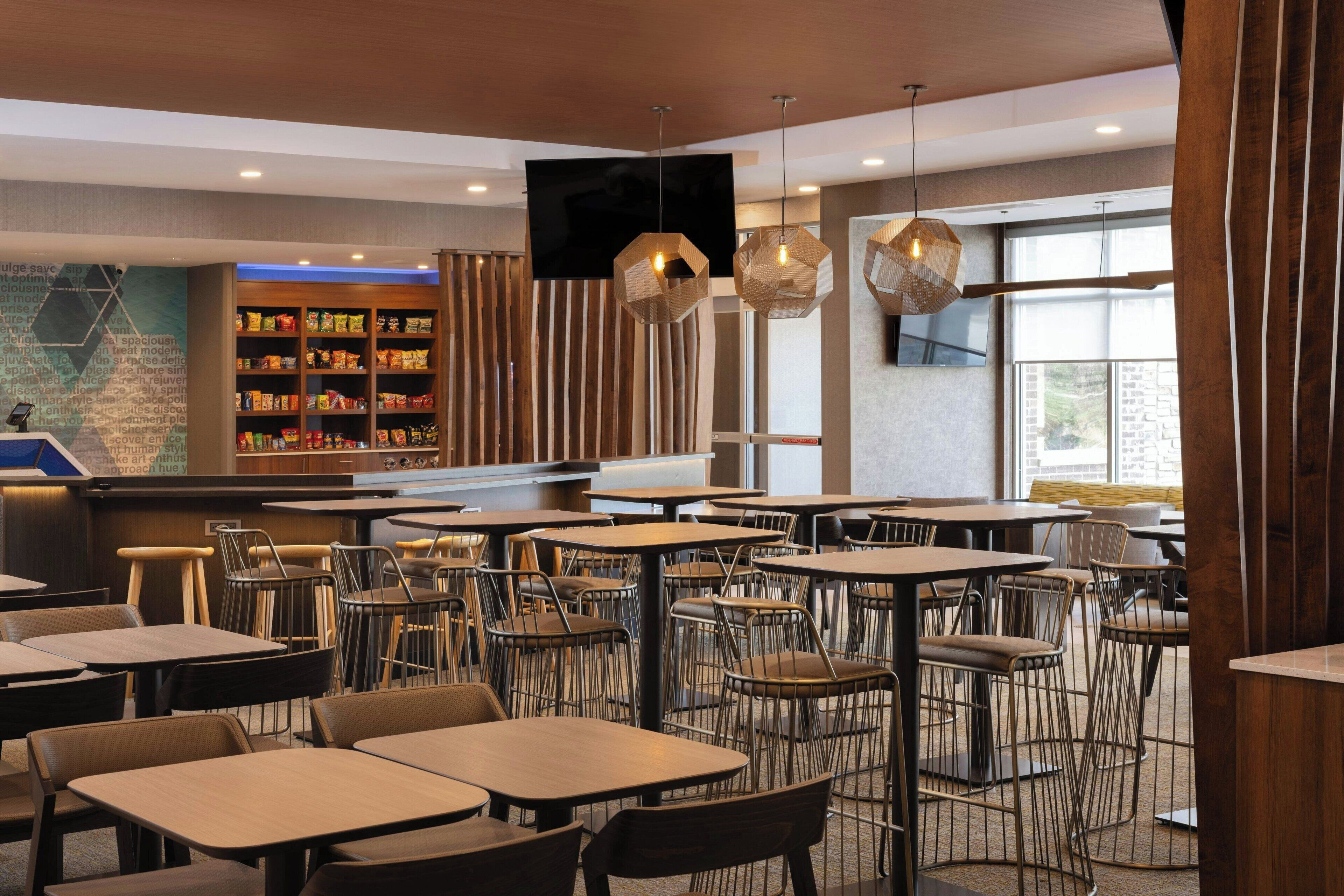 A modern restaurant with multiple tables and chairs, a bar area, and a large screen.