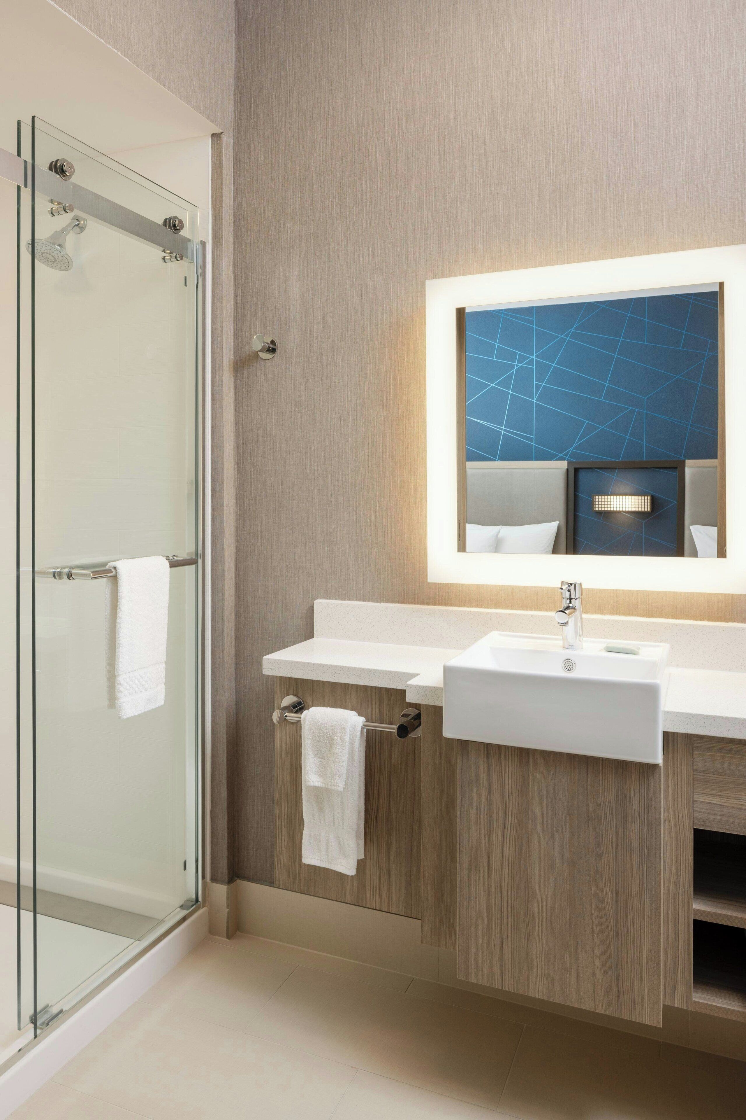 A modern bathroom with a glass shower enclosure, a white sink, and a mirror with a geometric light fixture.
