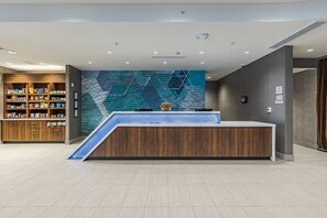 A modern reception area with a wooden reception desk, a blue geometric wall mural, and a snack kiosk to the left. - SpringHill Suites by Marriott Detroit Sterling Heights (Sterling Heights)