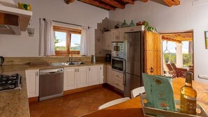 Una cocina con armarios blancos, lavavajillas de acero inoxidable, refrigerador y una ventana con cortinas.