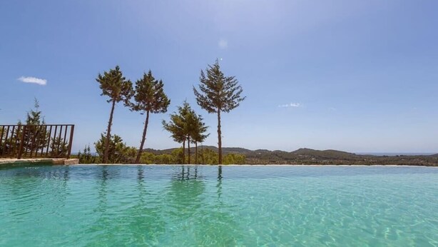 Una piscina cristalina con vistas a una playa y árboles al fondo.
