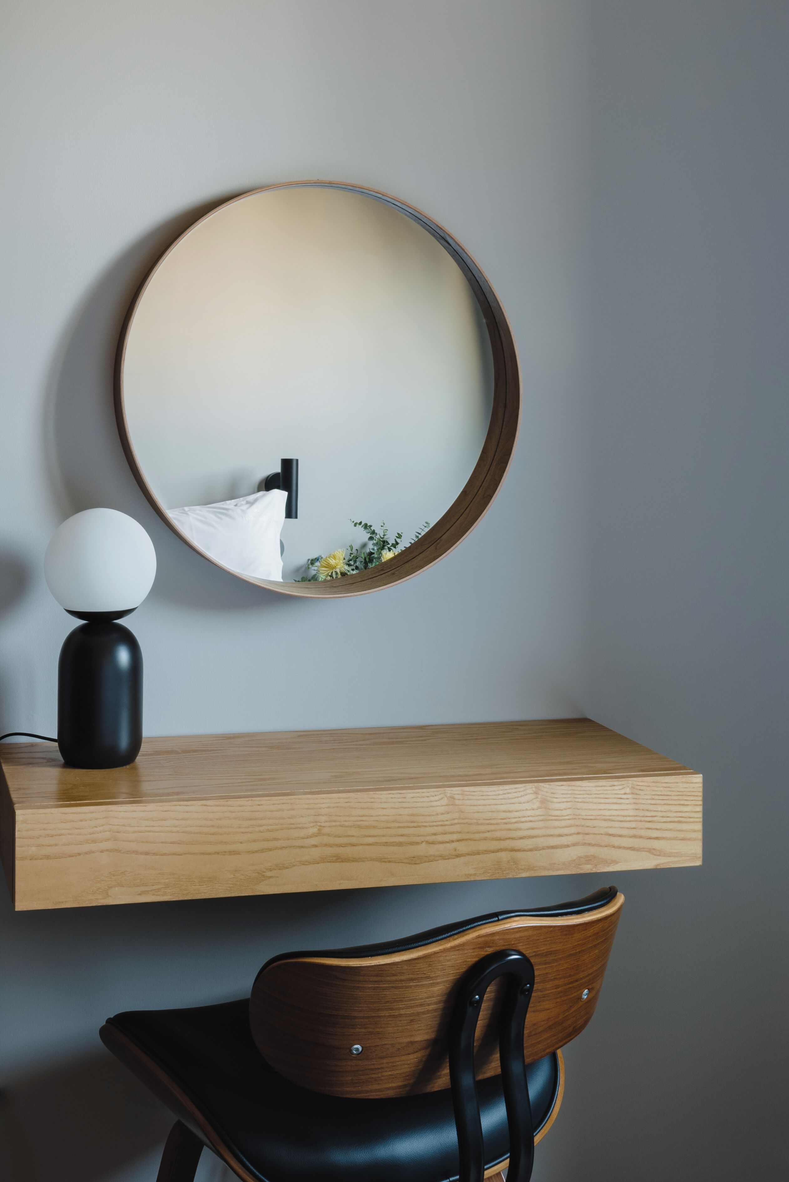 Una habitación moderna con un espejo redondo en una pared de madera, una lámpara negra y una silla de madera.