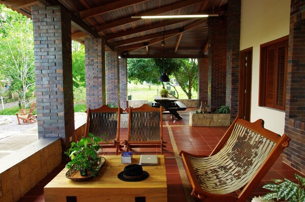 Un espacio de descanso al aire libre con columnas de ladrillo, muebles de madera y plantas en macetas.
