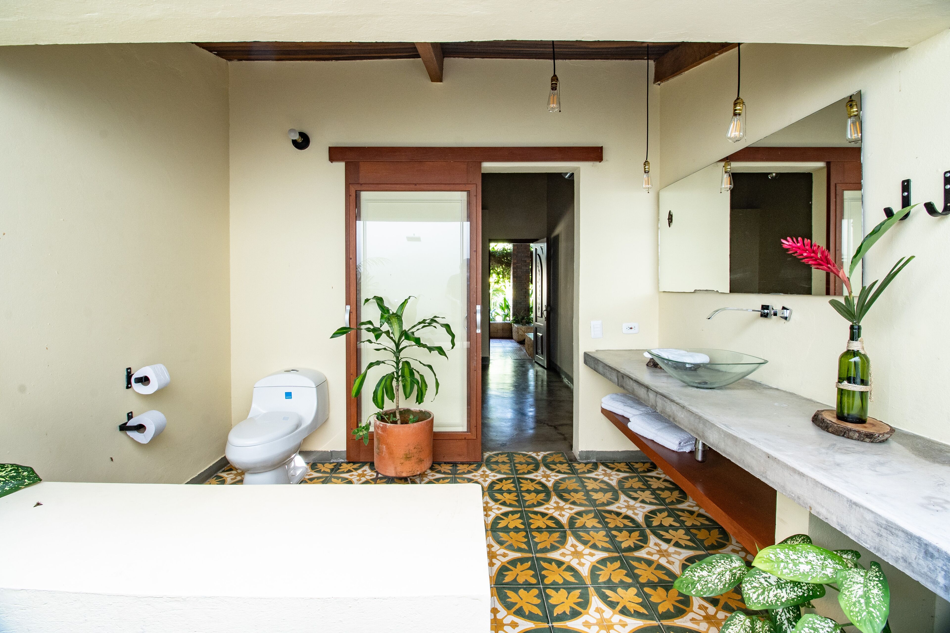 A bathroom with a toilet, sink, mirror, and potted plants.