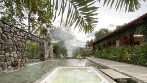 A hot spring area with a stone wall, a wooden deck, and lush greenery. - Hacienda Boutique  (Restrepo)