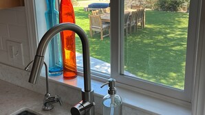 A kitchen sink with a modern faucet, a glass soap dispenser, and colorful vases on the windowsill.