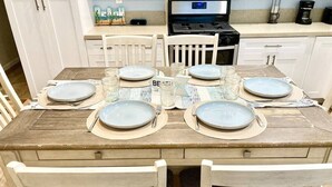 A dining table set with plates, glasses, and cutlery, surrounded by white chairs. - Monthly Coastal Stay - Fully Furnished 3BR/2BA Home (Oceanside)