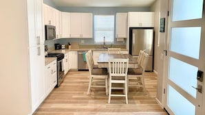 A modern kitchen with white cabinets, a dining table, and chairs. - Monthly Coastal Stay - Fully Furnished 3BR/2BA Home (Oceanside)