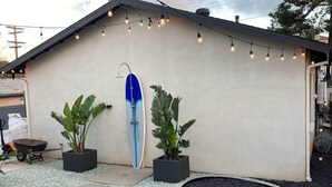 A building with a surfboard mounted on the wall, potted plants, and string lights. - Monthly Coastal Stay - Fully Furnished 3BR/2BA Home (Oceanside)
