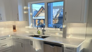 A modern kitchen with white cabinets, a stainless steel dishwasher, and a window overlooking a snowy landscape.