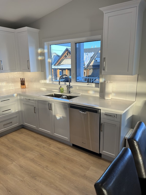 A modern kitchen with white cabinets, a stainless steel dishwasher, and a window overlooking a snowy landscape. - Whispering Pines Lakeside Resort - with A/C-Golf-Pool-Gym-Beach-Restaurant-Parks (Red Deer County)