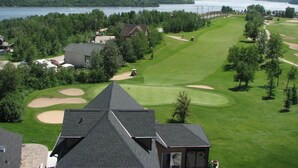 A golf course with a clubhouse, a lake, and surrounding wooded areas.