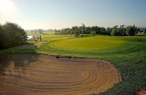 Un campo da golf con un green curato, una zona sterrata con motivi circolari e un cielo sereno.