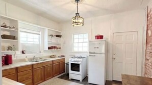 A compact kitchen with white cabinets, a stove, a refrigerator, and a dining area with a table and chairs. - House - Wetumpka (Wetumpka)