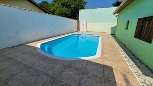 A rectangular swimming pool with a tiled deck, surrounded by walls with a light green and white color scheme.