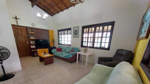 A living room with a sofa, a TV, a fan, and a window with blinds.