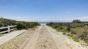 A sandy path leading to a beach with a white fence on the left and a wooden structure on the right. - Emerald Isle Getaway w/ Decks & Beach Views! (Emerald Isle)