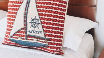 A bed with a wooden headboard, a quilted white bedspread, and a red and white patterned pillow with a sailboat design and the word "NAUTIC".