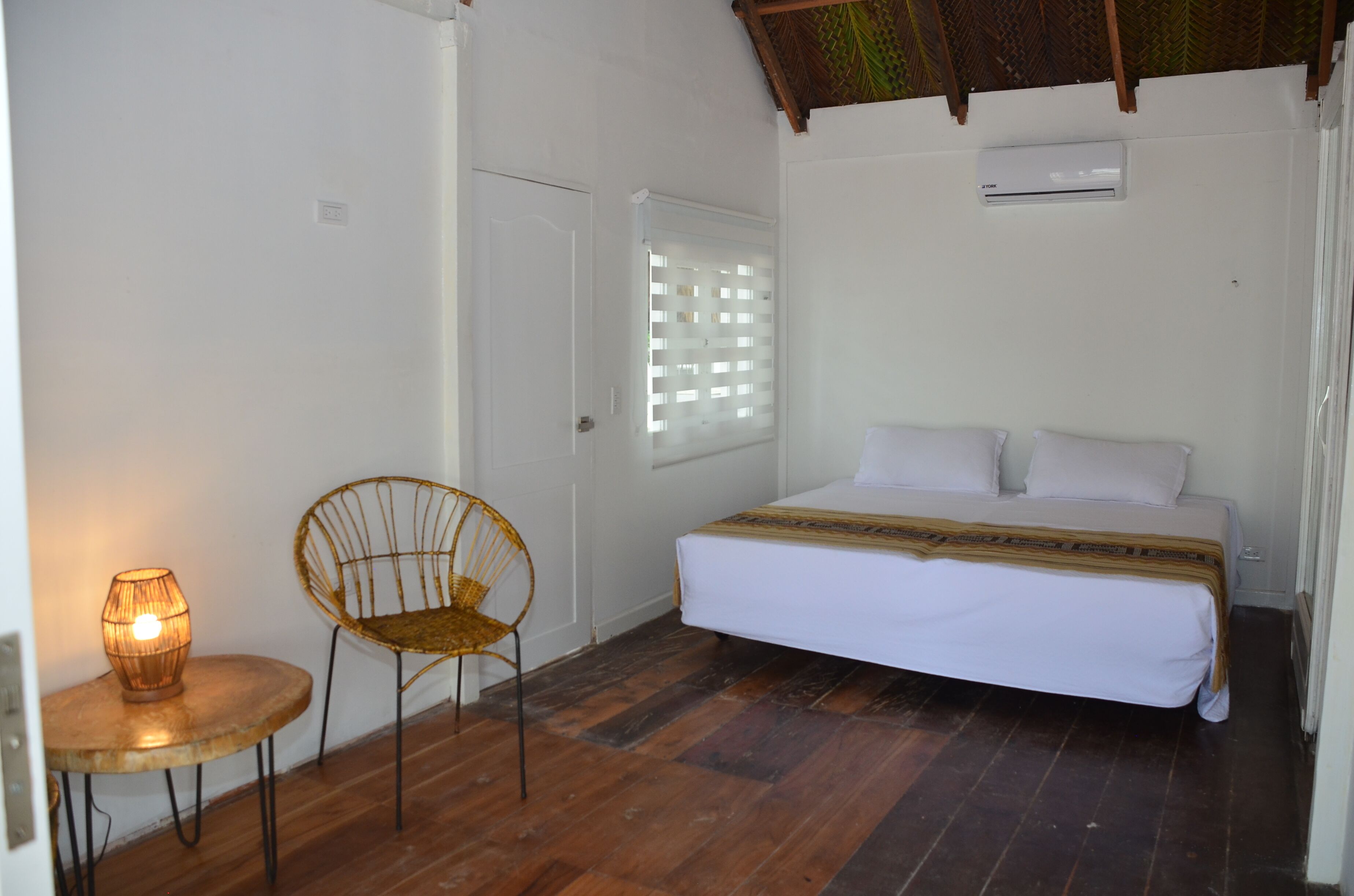A bedroom with a bed, a chair, a table with a lamp, and an air conditioning unit.