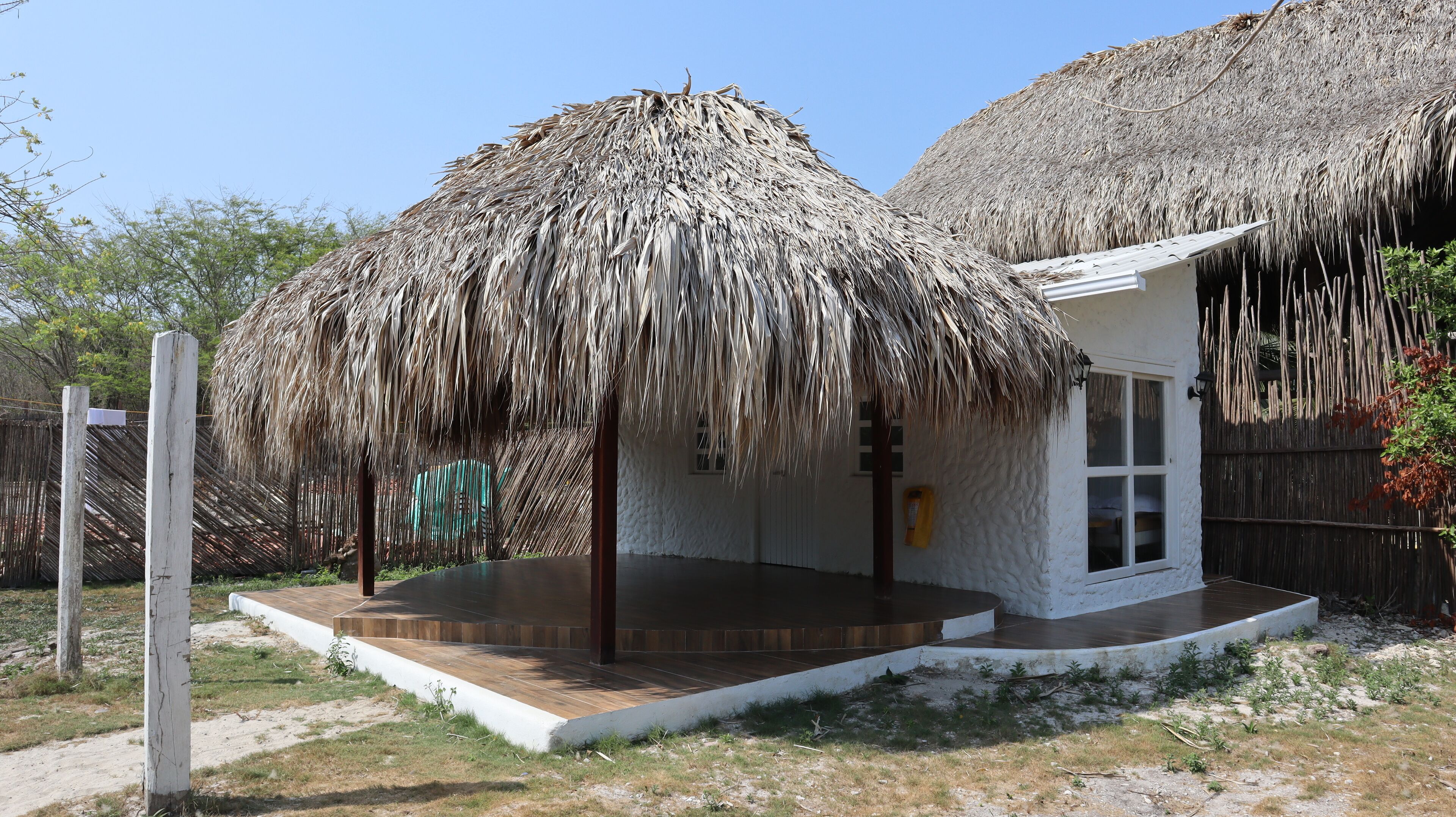 Uma construção com telhado de palha, fachada branca, um pequeno alpendre e uma janela.