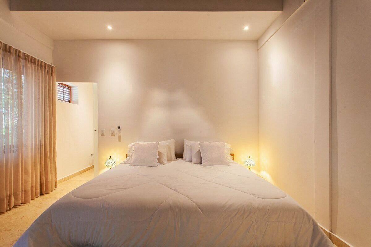 A bedroom with a large bed, bedside lamps, and a window with curtains.