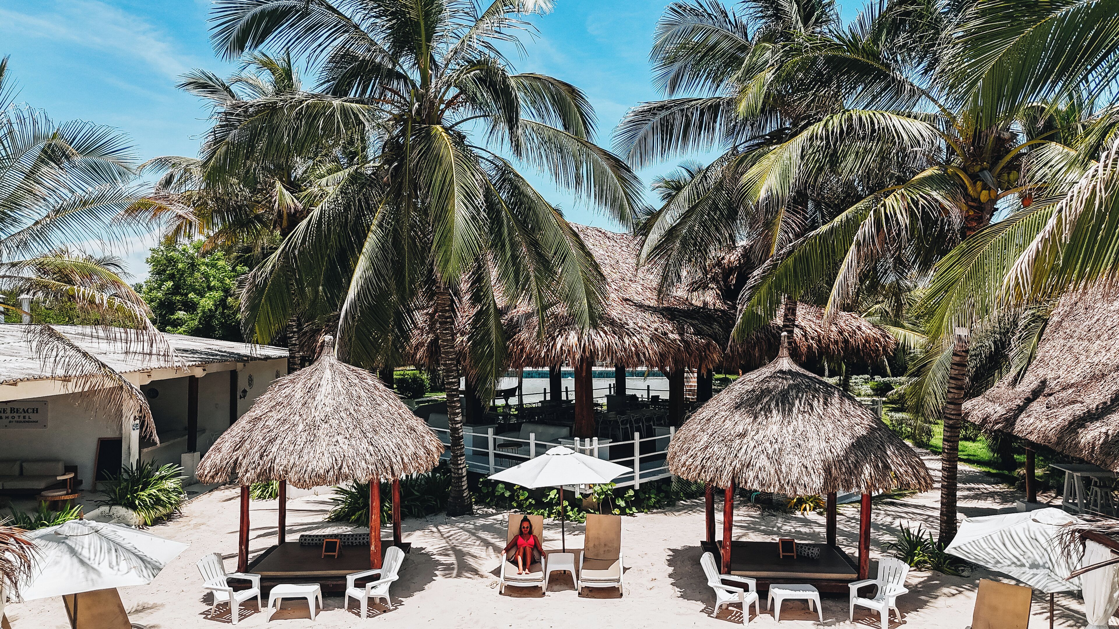 A beachside resort with thatched umbrellas, white lounge chairs, and a stage for events.