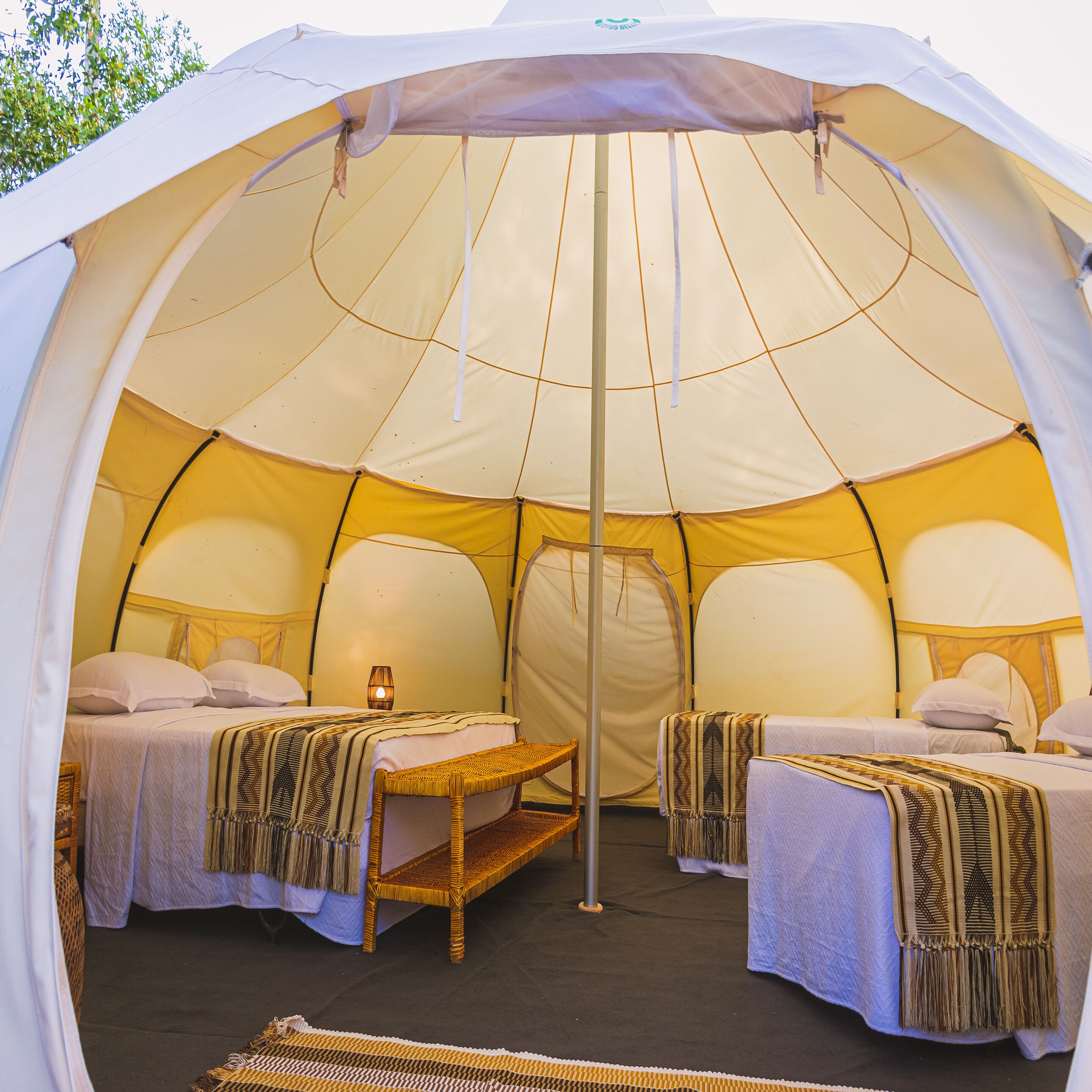 A tent with two beds, a central table, and a hanging light fixture.