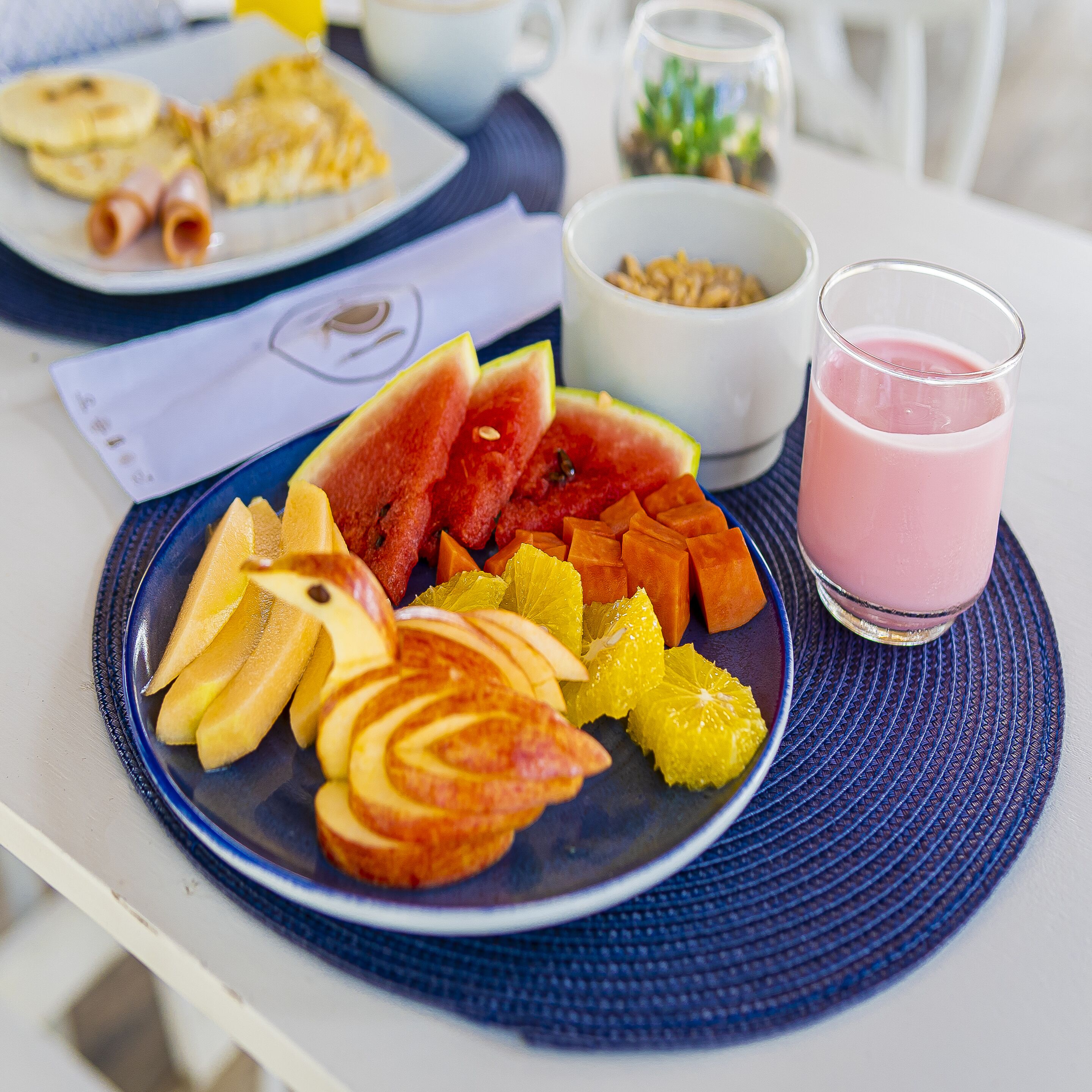 A breakfast plate with sliced fruits and a glass of pink smoothie.