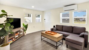 Un salon moderne avec un téléviseur à écran plat, un canapé gris, une table basse en bois et une plante en pot.