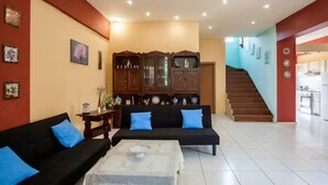 A spacious living area with a black sofa set, a wooden cabinet, and a staircase leading to another room.