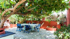 An outdoor patio with a table and chairs under a tree, surrounded by potted plants and a red wall.