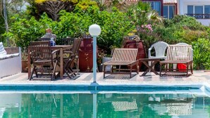 A poolside area with wooden lounge chairs, a table, and a lamp post.