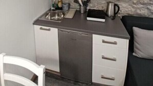 Cocina compacta con pared de piedra, microondas, pileta y un mueble pequeño con puertas de vidrio.
