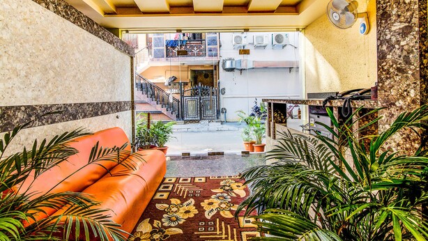 A hotel lobby with a marble wall, a red sofa, potted plants, and a patterned rug. - FabHotel Emara Boutique - Near Koramangala (Bengaluru)