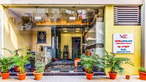 A hotel entrance with a glass door, potted plants, and a signboard. - FabHotel Emara Boutique - Near Koramangala (Bengaluru)