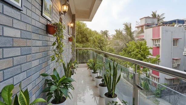 A balcony with potted plants, a glass railing, and a view of surrounding buildings. - FabHotel All In One Saltlake (Barasat)