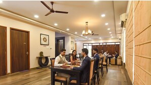 A dining area with wooden flooring, ceiling fans, recessed lighting, and a long table with chairs. - FabHotel All In One Saltlake (Barasat)