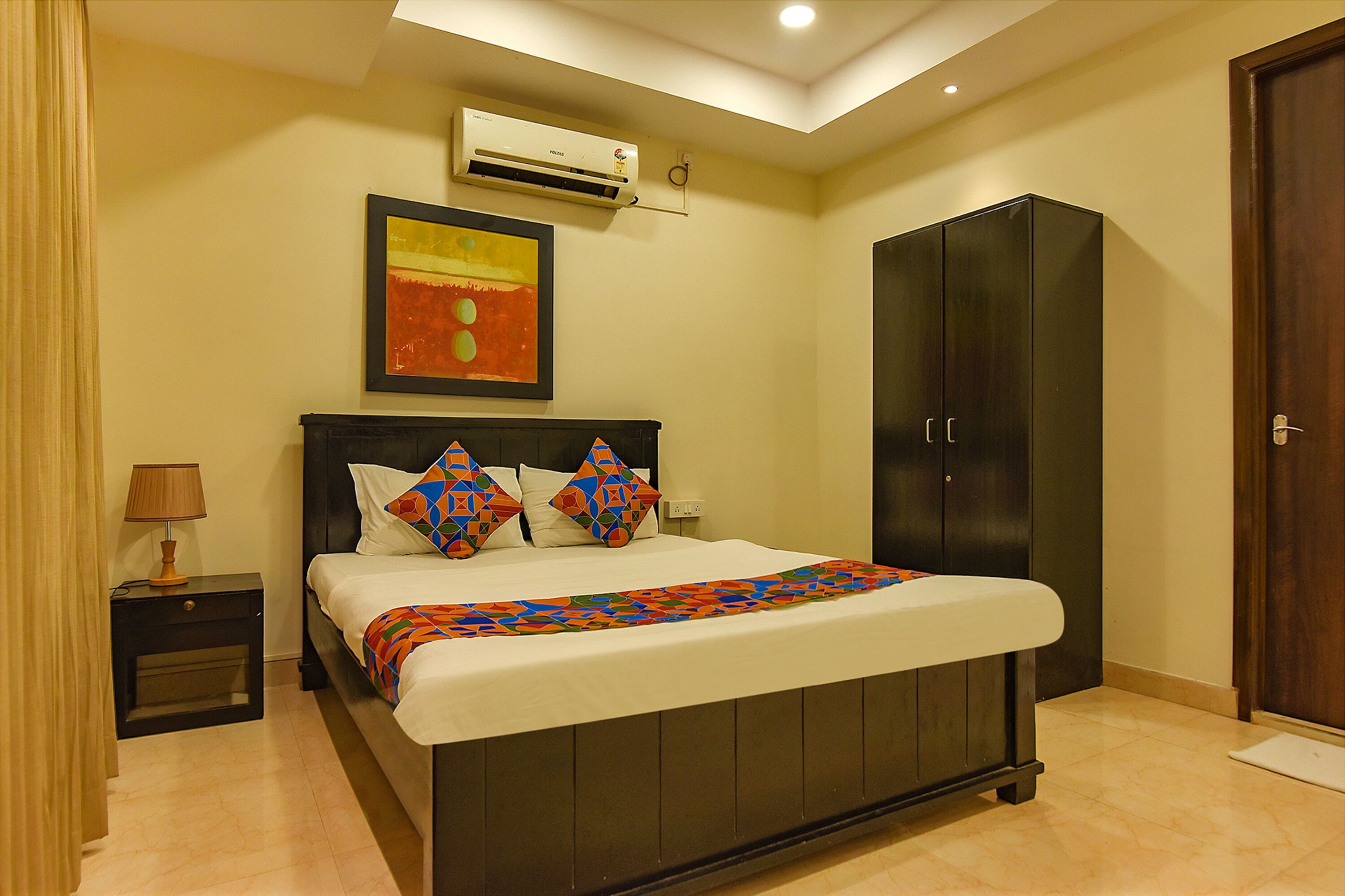 A bedroom with a bed, a wardrobe, a nightstand with a lamp, and an air conditioning unit on the wall.