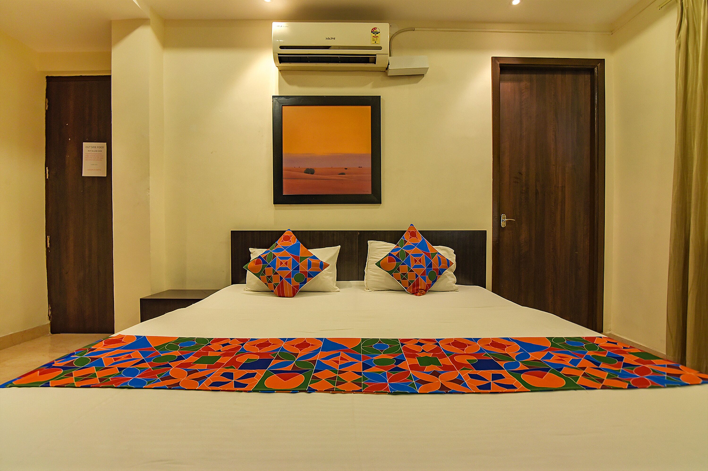 Una habitación de hotel con una cama, dos almohadas, un cuadro en la pared y un equipo de aire acondicionado.