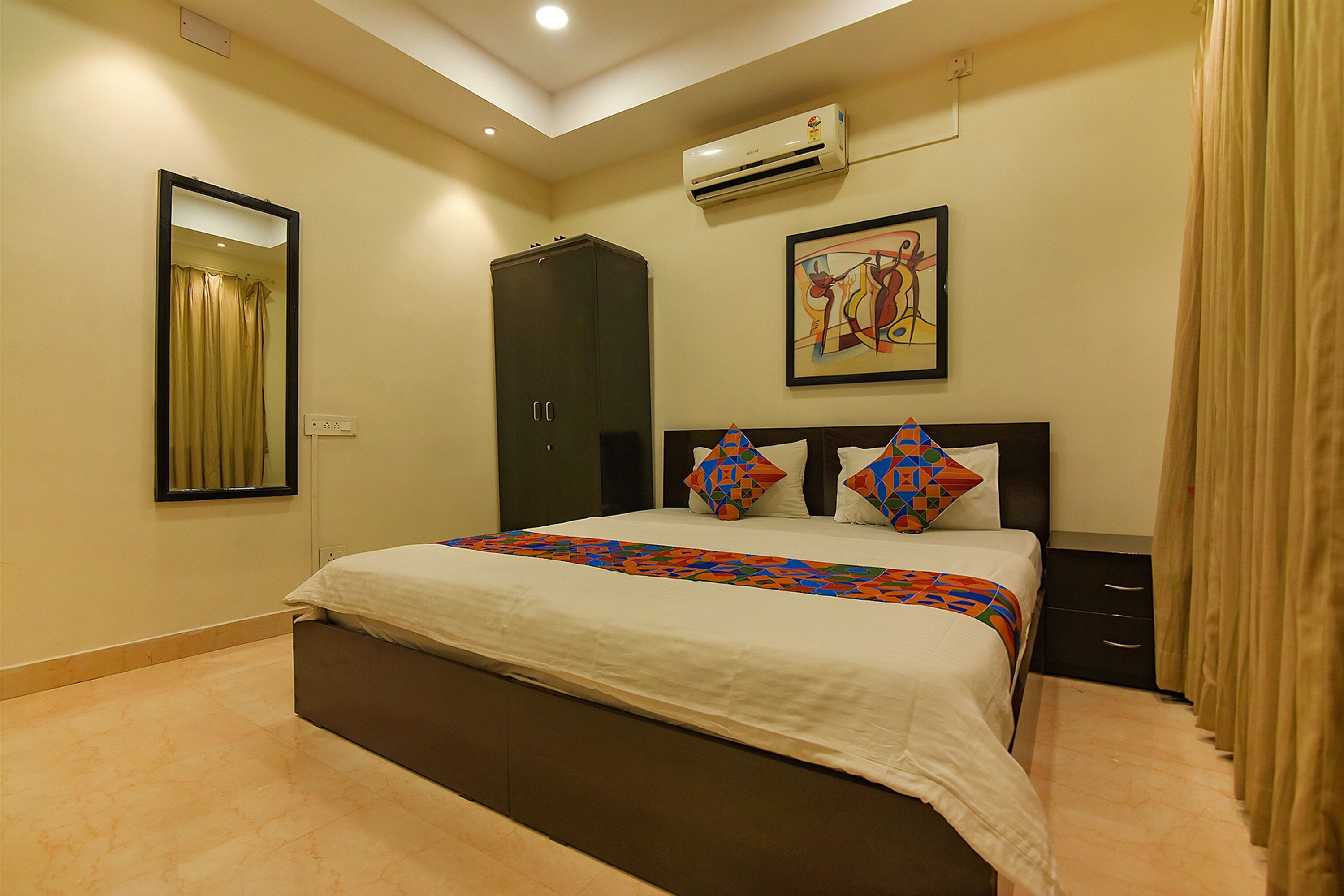 A bedroom with a bed, a wardrobe, a ceiling light, an air conditioner, and a painting on the wall.