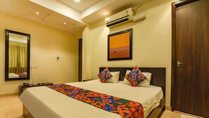 A hotel room with a bed, a nightstand, a mirror, an air conditioner, and a door. - FabHotel All In One Saltlake (Barasat)