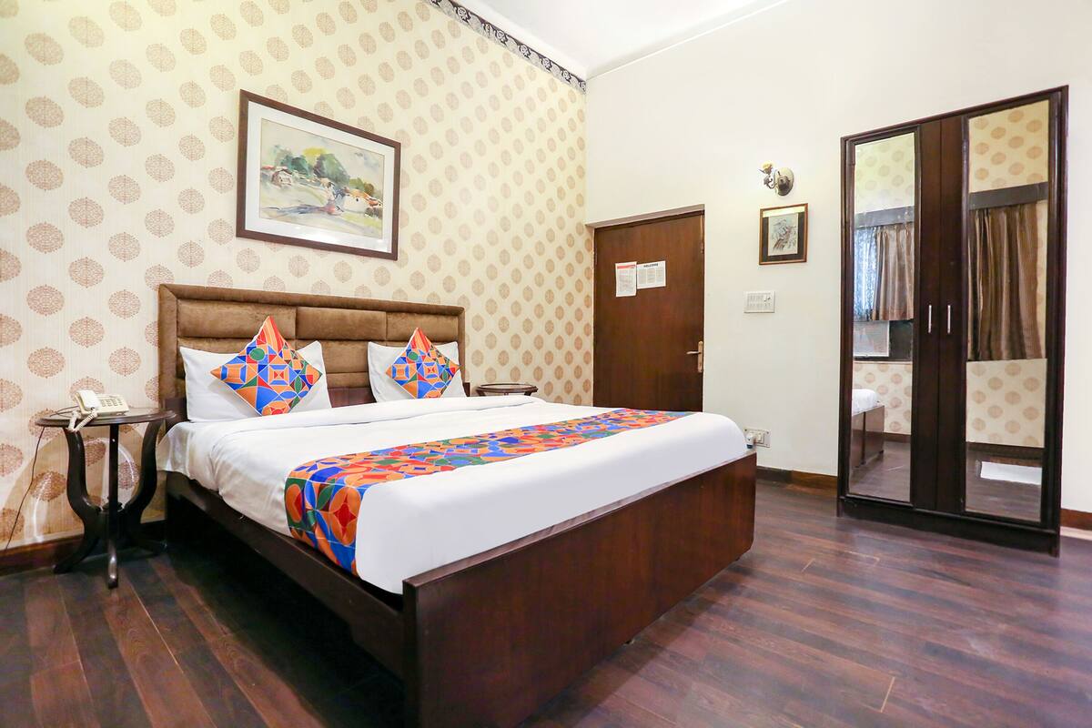 A hotel room with a large bed, a bedside table with a phone, a door with a mirror, and patterned wallpaper.