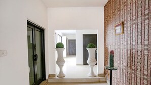Un couloir avec une porte en verre, deux piédestaux blancs ornés de plantes, un mur à motifs et une petite table sur laquelle est posé un vase.