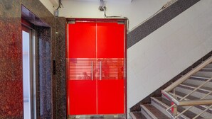 Una puerta roja de ascensor con una celosía metálica, un muro de mármol y una escalera con barandillas de metal.