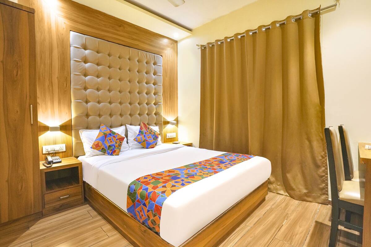 A hotel room with a large bed, wooden headboard, two bedside tables with lamps, a nightstand, and a chair.