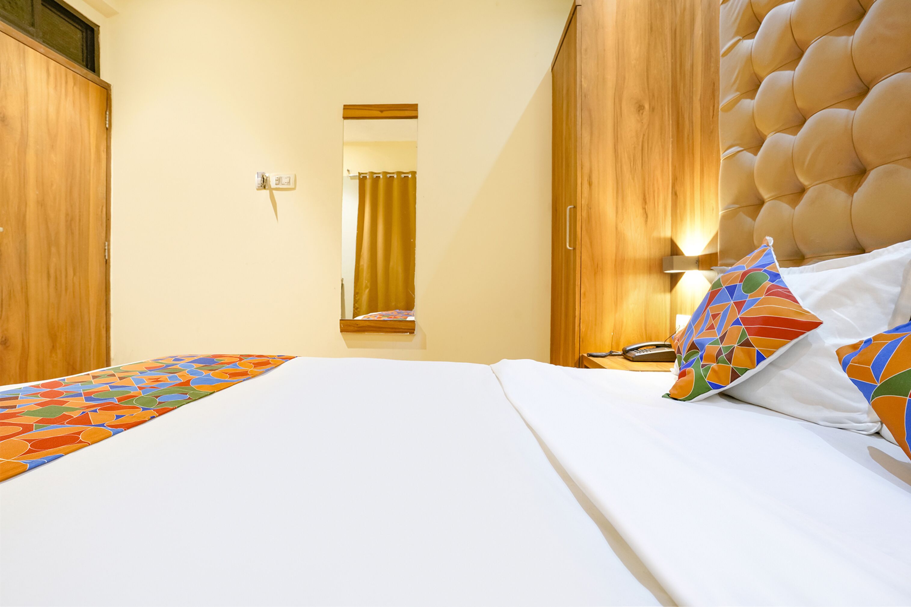A hotel room with a large bed, wooden wardrobe, and a mirror.