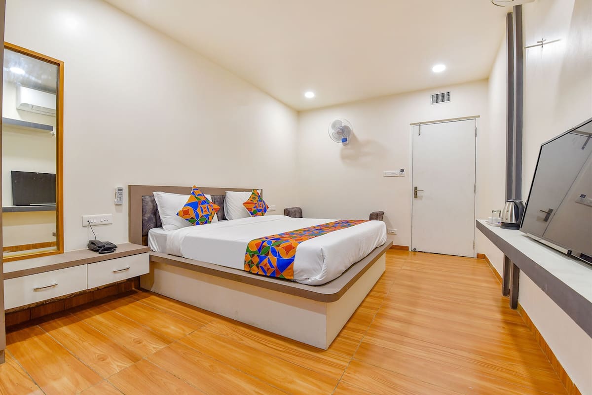 A bedroom with a bed, bedside table, mirror, and a TV.