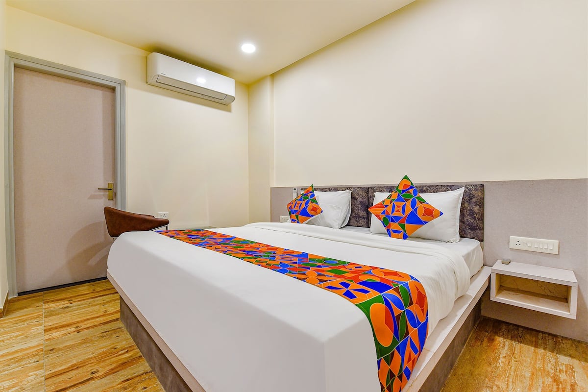 A hotel room with a bed, a chair, a nightstand, an air conditioning unit, and a door.