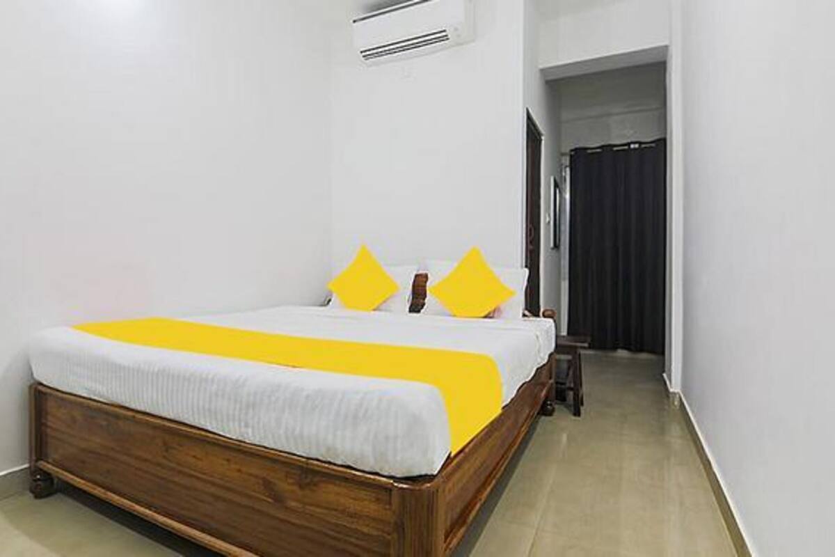 A single bed with a wooden frame and a white mattress, flanked by two yellow pillows.