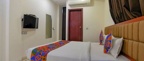 A hotel room with a bed, a bedside table with a phone, an air conditioning unit, a television, and a door.